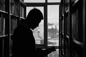 A moody silhouette of a man reading in a library, capturing solitude and contemplation.