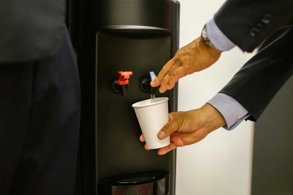 Man in business attire pouring water into a white cup from a dispenser.